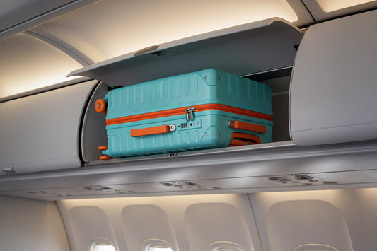 Lightweight turquoise Tavoxda suitcase with orange accents in airplane overhead bin