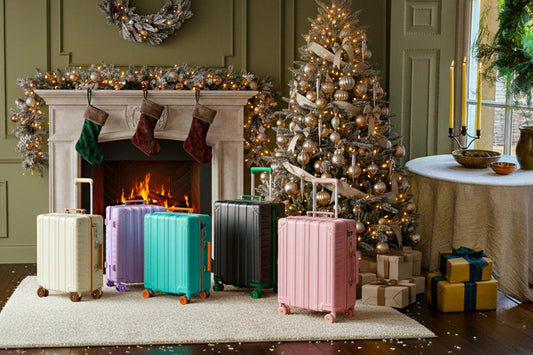 Tavoxda lightweight luggage in assorted colors by a Christmas tree and festive fireplace setting